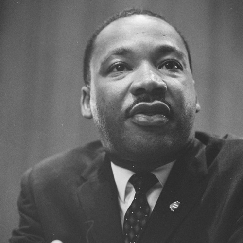 Head-and-shoulders portrait of Martin Luther King leaning on a lectern. 1964